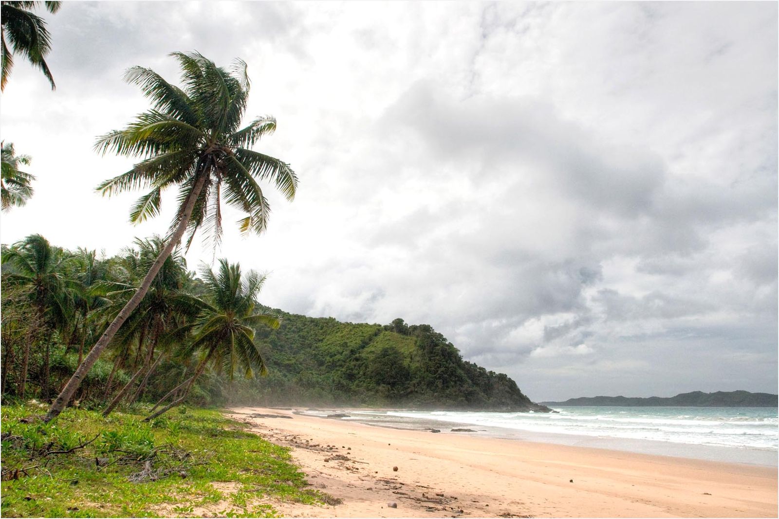 Waves rolling onto the wide golden sand at Duli Beach, El Nido